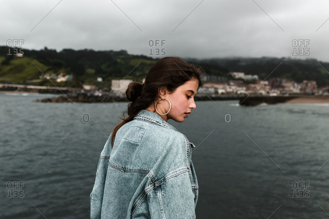 Contemplative brunette woman in vintage denim jacket before stormy weather at the beach