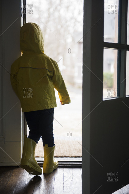 Girl (2-3) in rubber boots and rain cape standing at open door