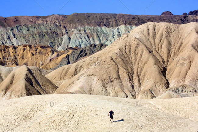 Person on barren slope in mountain range with various minerals and colors in Death Valley