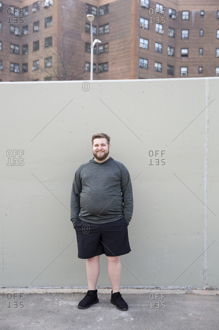 Full length portrait of overweight man with hands in pockets standing against wall in city