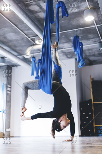 Full length of young woman practicing aerial yoga while hanging from hammock in gym