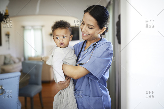 Smiling pediatrician carrying baby boy while standing at home