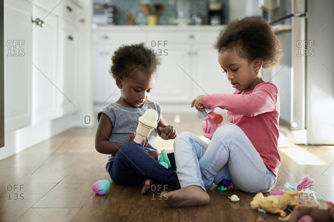 Sisters playing with ice cream toys while sitting on hardwood floor at home
