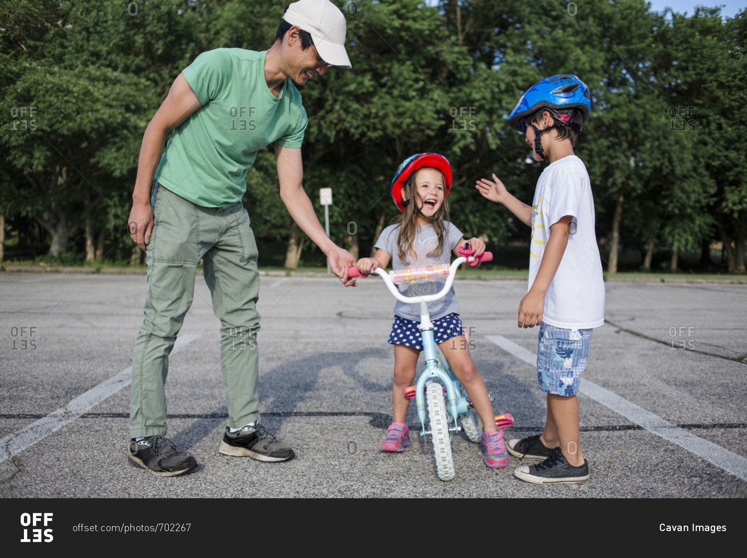 Cheerful girl learning cycling with father and brother at playground