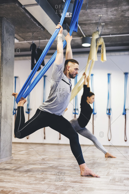 Friends stretching using hammocks while practicing aerial yoga in gym