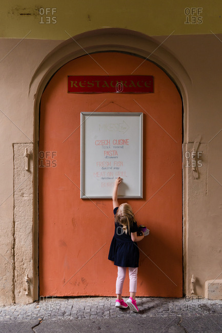 Rear View Of Little Girl Touching Menu Board On Restaurant Door