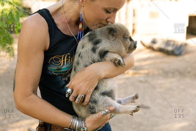 Young woman holding and kissing a spotted baby pig