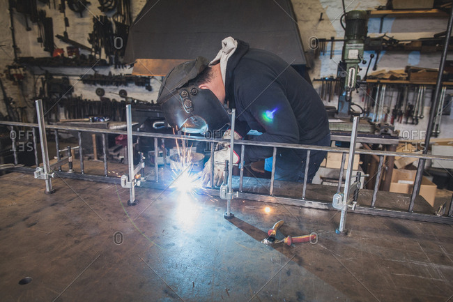 A blacksmith wears safety gear and is welding a metal construction in a metalsmith's workshop