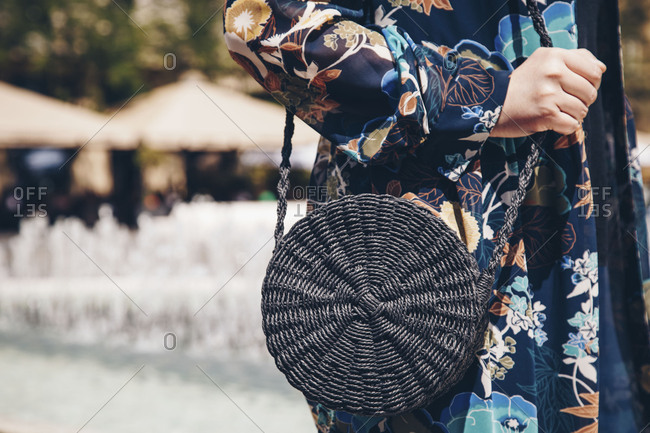 Street style fashion detail, close-up of a woman wearing a floral kimono and holding a black round straw purse