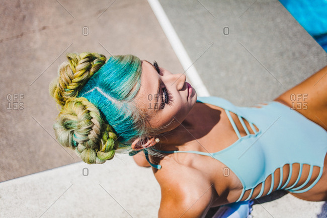 High angle side view of sunbathing model in pastel swimwear and neon dyed braids