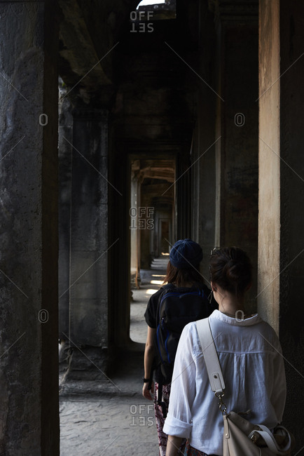 Japanese female travelers walking across corridor inside temple of Angkor Wat, Cambodia