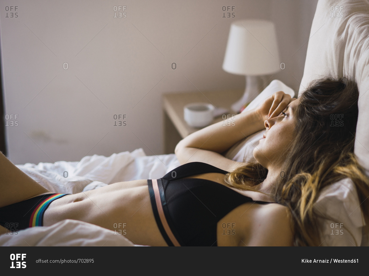 Daydreaming young woman in underwear lying on bed stock photo - OFFSET