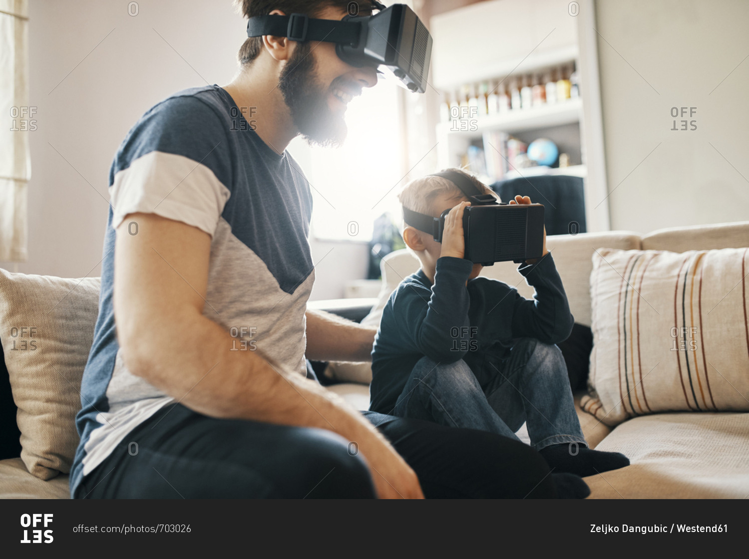 Father and little son sitting on the couch at home wearing virtual reality glasses