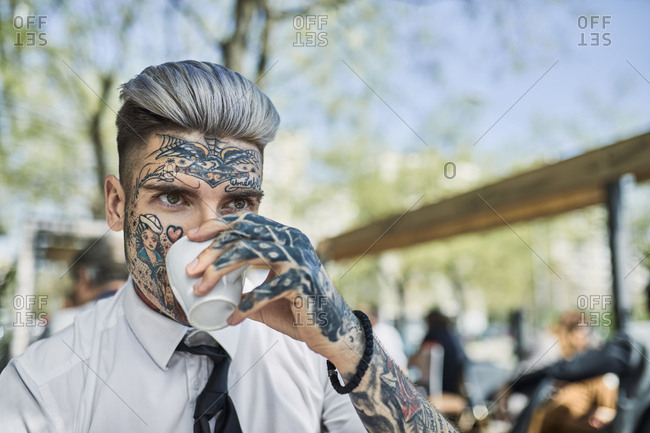 Young businessman with tattooed face- drinking coffee stock photo - OFFSET