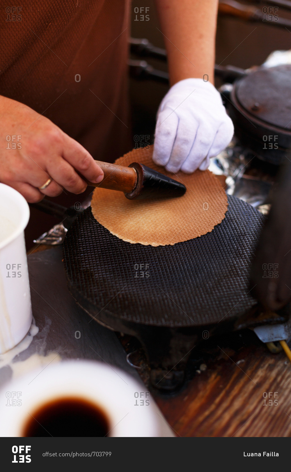 Ice cream vendor preparing flat waffle before rolling into cone shape