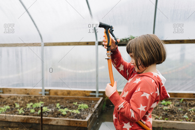 Side profile of little girl spraying water hose in greenhouse