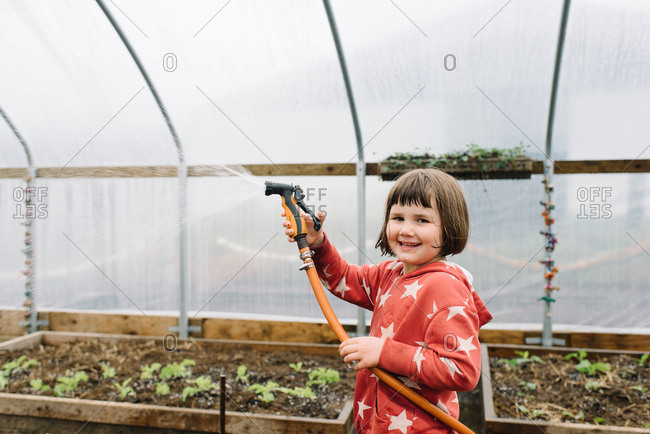 Young girl in greenhouse garden smiling with water house