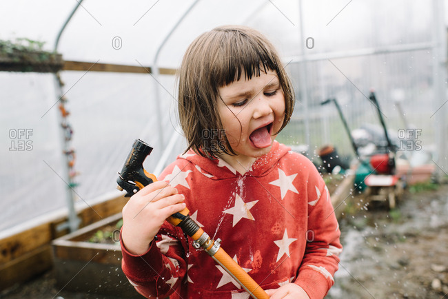 Brunette girl drinking from water hose while gardening in greenhouse