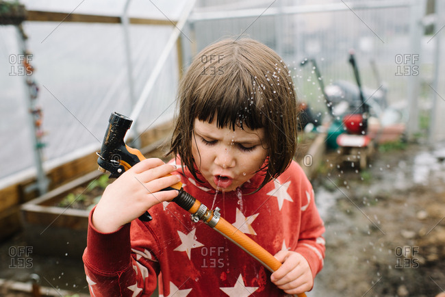 Young girl playing with splashing water hose in greenhouse