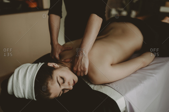 Massage therapist working on shoulders and neck area of female client laying on front