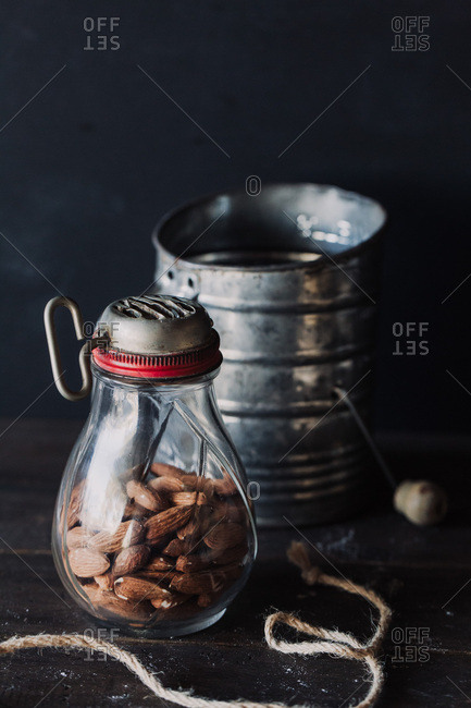 Almonds in antique glass grinder and tin can on dark table against dark background