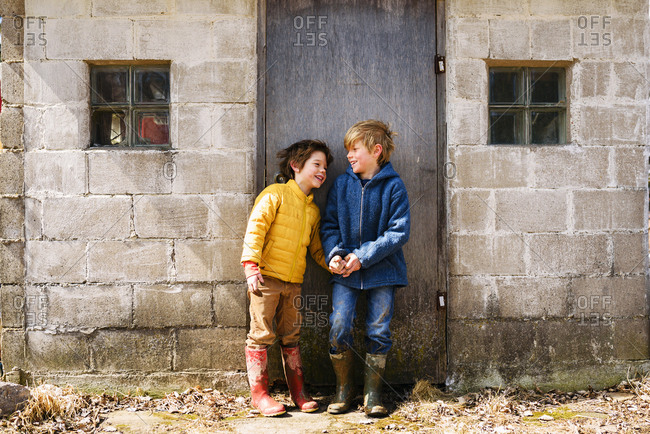 Two young brothers grubby from playing in the mud sharing a joke outside shed