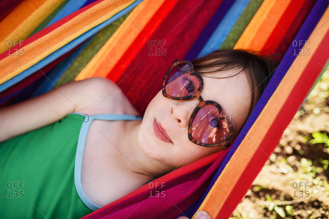 Young girl in heart-shaped sunglasses relaxing in a colorful hammock
