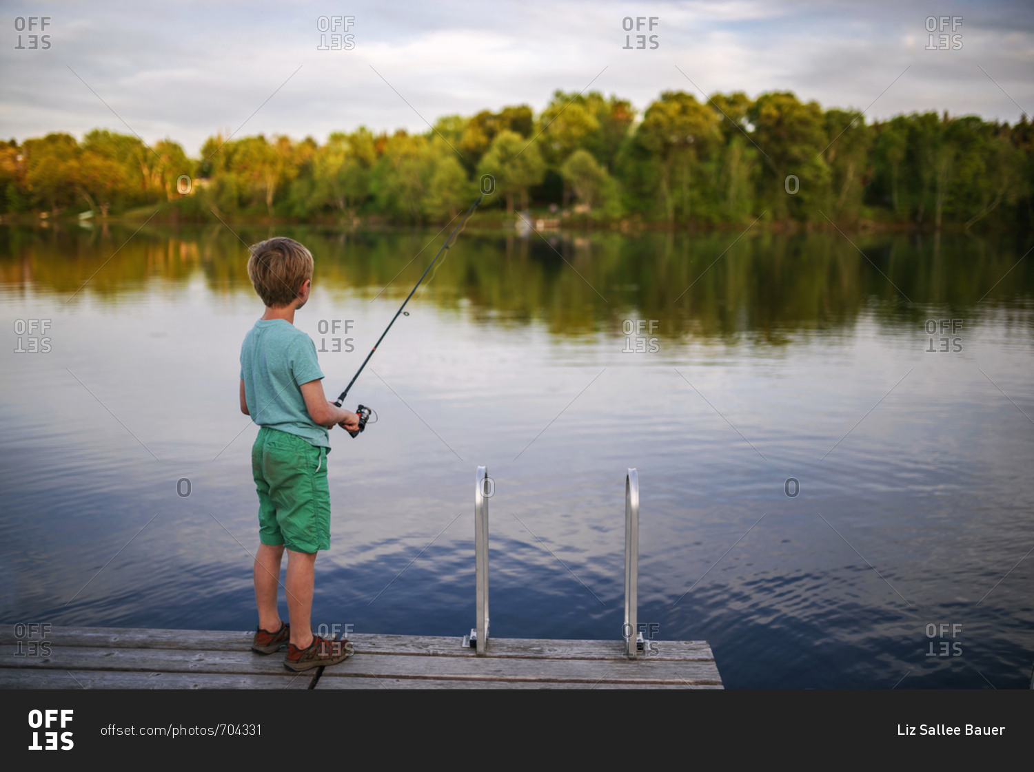 A young boy fishing alone off a dock stock photo - OFFSET