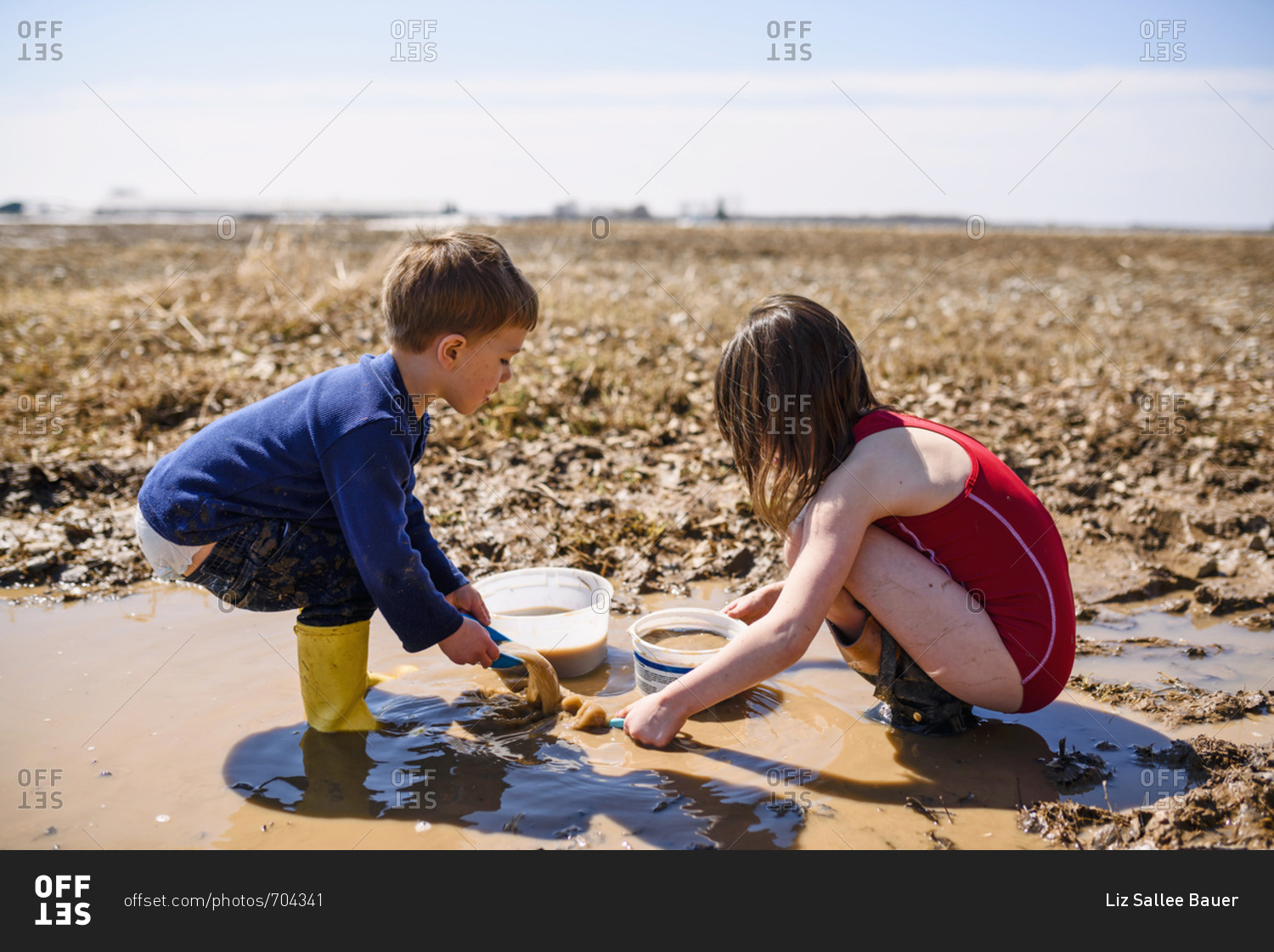 Two young kids playing in mud puddles in a field stock photo - OFFSET