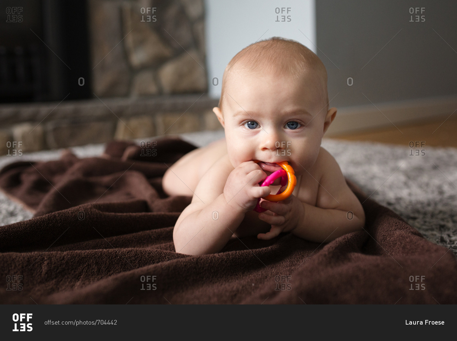 Naked baby chewing on toy while lying on blanket