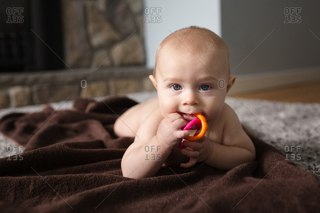 Naked baby chewing on toy while lying on blanket