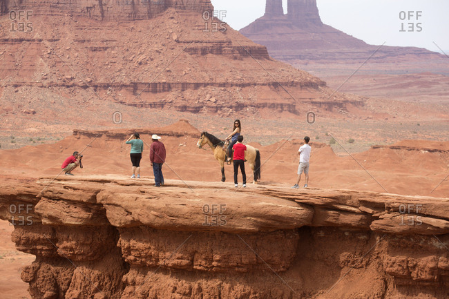 Monument Valley, Utah, USA - May 6, 2018: Tourists posing for pictures on mesa with American Indian and horse