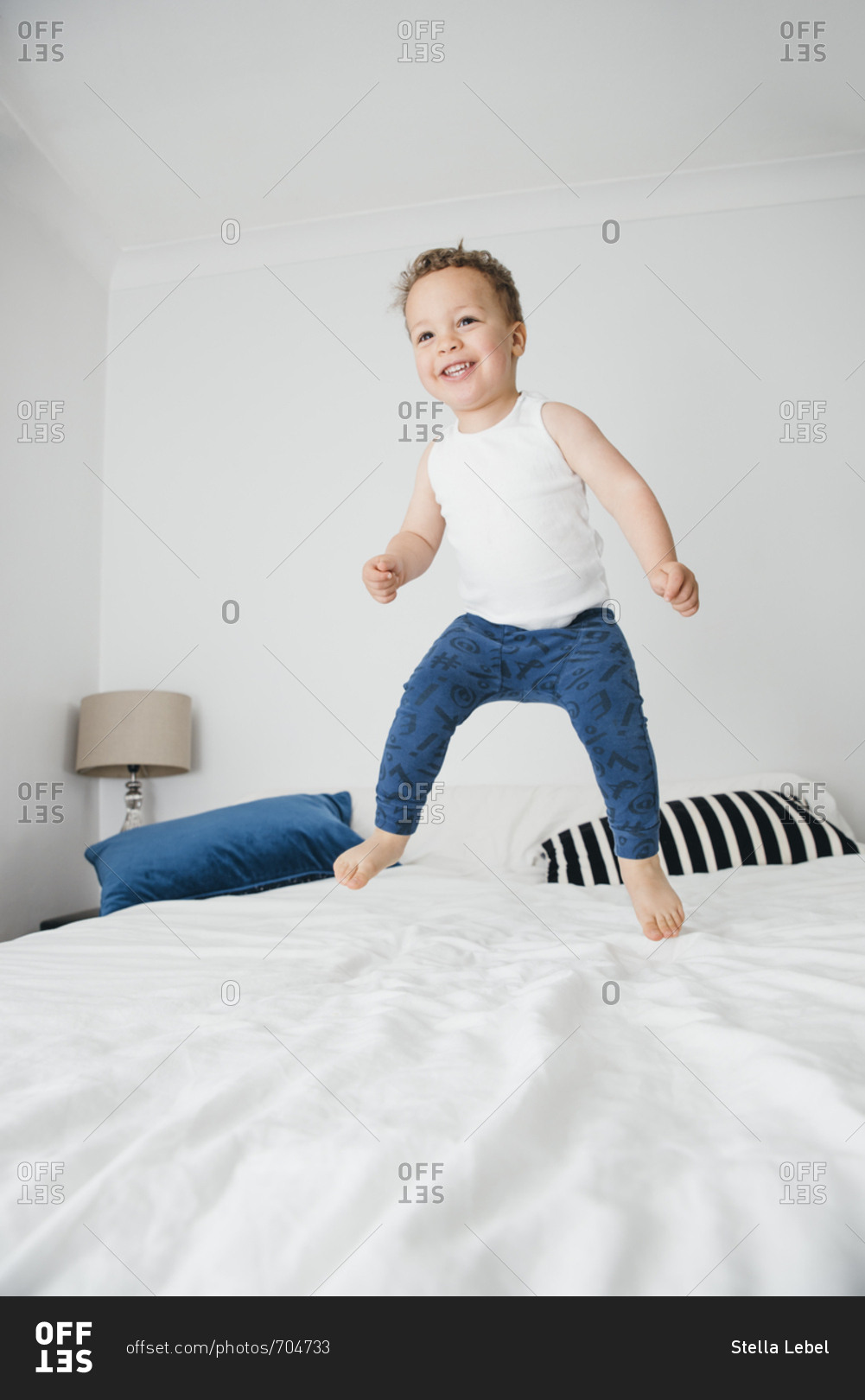 Smiling toddler jumps on bed stock photo OFFSET