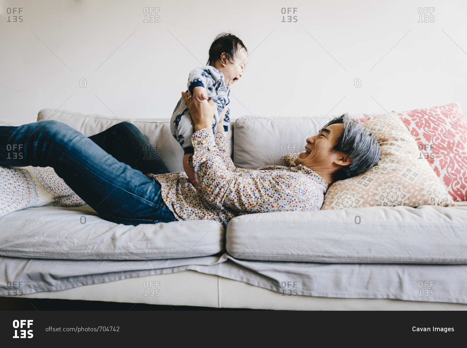 Happy grandfather playing with grandson while lying on sofa at home ...