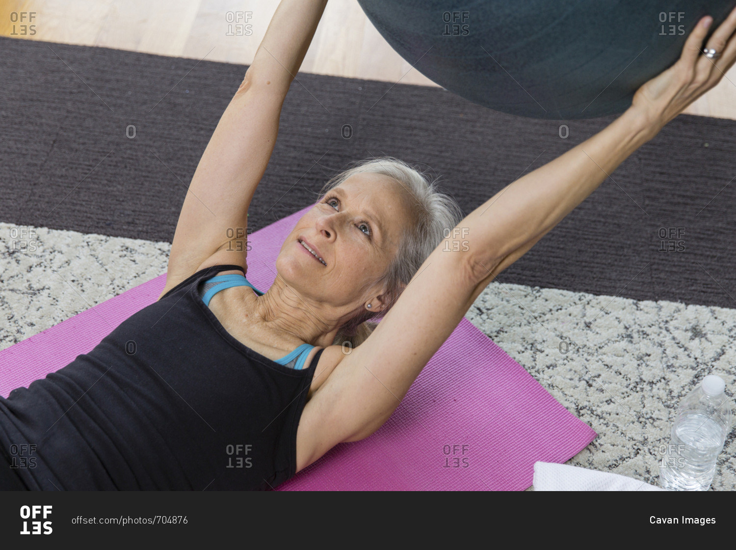 Senior woman holding fitness ball while lying on exercise mat at home