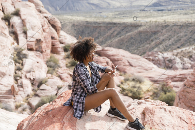 High angle view of woman using smart phone while sitting on rock formation
