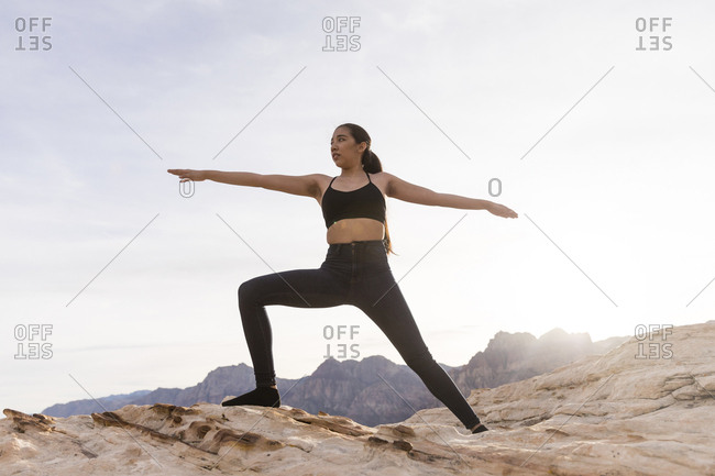 Woman practicing warrior pose on rock formation against sky