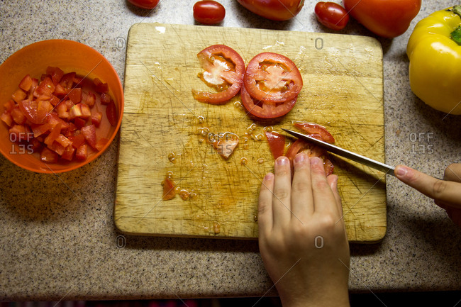 Looking down on small pair of hands dicing tomatoes on chopping board