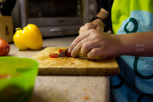 Low angle view of pair of children's hands slicing cherry tomatoes in kitchen