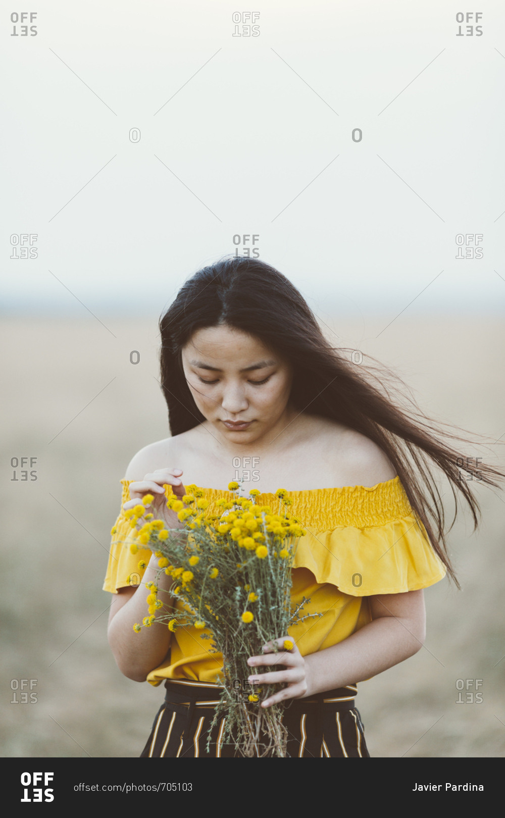 Young Asian woman in field holding yellow flowers