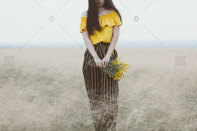Young Asian woman in field holding yellow flowers