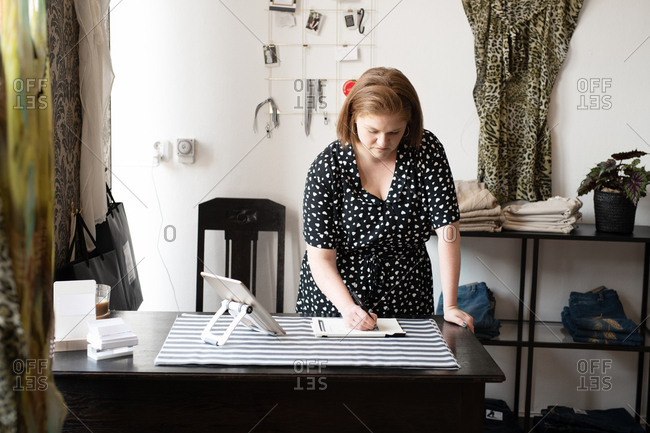 Shop owner writing down note while working in her boutique