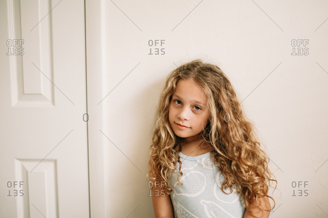 Young Girl With Long Curly Blonde Hair Smirking Against Wall Stock