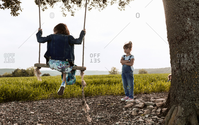 A little girl plays on a swing while her sister waits to play