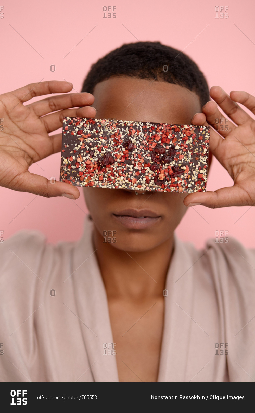 Conceptual portrait of young Black woman with short haircut hiding her eyes with smartphone in glittery case on pink background
