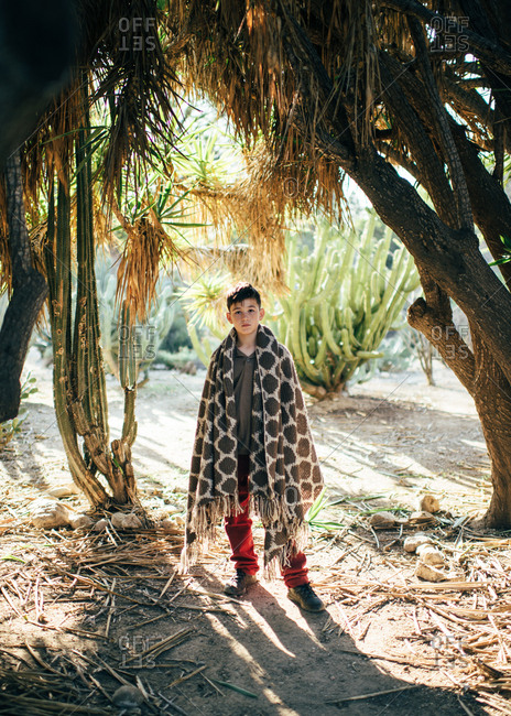 Boy standing along in shade with woven blanket