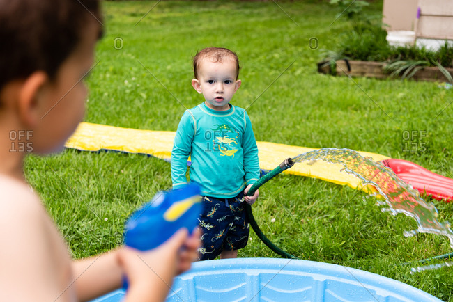 Young boy in swim wear holding water hose looking at brother holding squirt gun