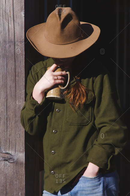 Cowgirl leaning on wooden beam while sipping coffee