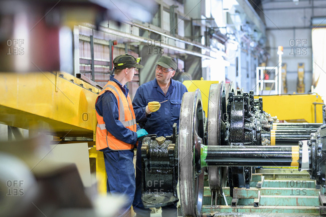 Engineer instructing apprentice with locomotive wheels in train engineering factory