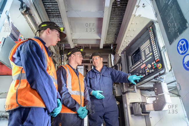 Engineer instructing apprentices at controls of locomotive wheel lathe in train engineering factory